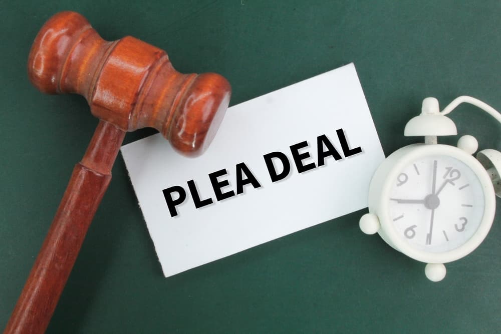 Judge's gavel, bell clock and white paper with the words plea deal.